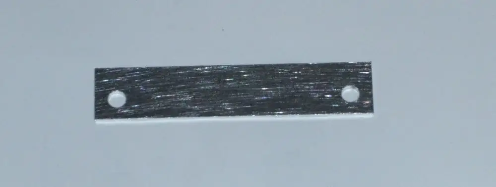 Metallstreifen mit zwei Löchern, möglicherweise zur Befestigung, auf einem hellen Hintergrund. Produkt könnte mit Daikin Altherma 3 R W in Verbindung stehen.